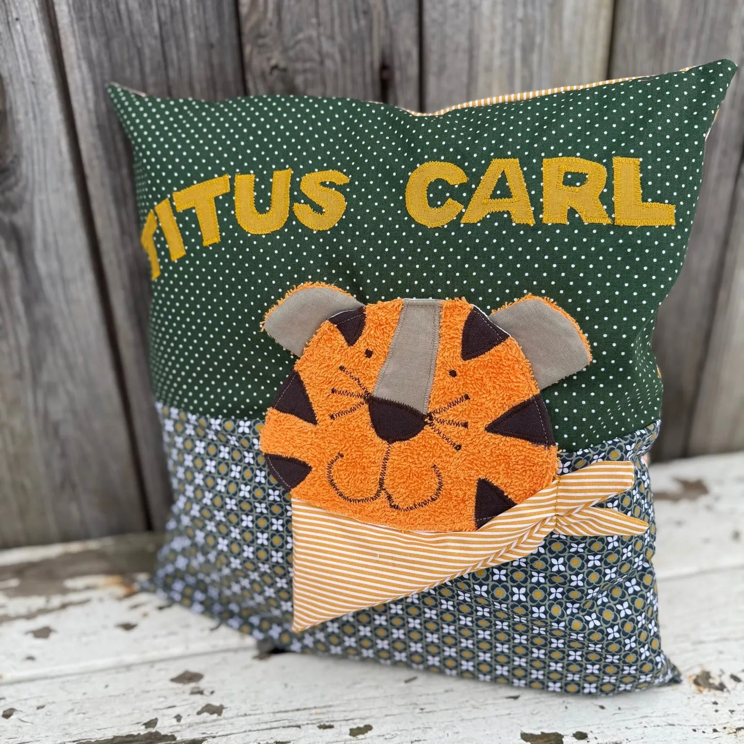 Handgenähtes Kinderkissen personalisiert, gestaltet grün mit weißen Punkten im oberen Teil, grünes Retromuster im unteren Teil. Auf dem Kissen ist eine Tiger-Applikation in leuchtendem Orange.Fotografiert vor einem rustikalen Holzhintergrund