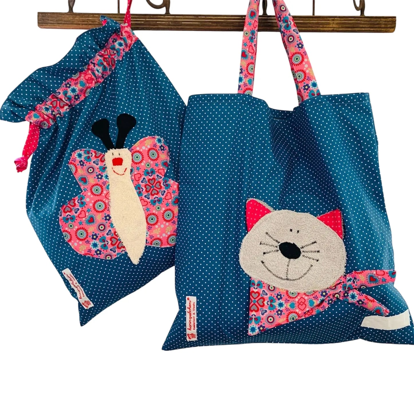 Handgemachtes Kita-Set bestehend aus einem blauen Wetbag mit Schmetterlingsmotiv und einem passenden Garderobenbeutel mit Katzenapplikation- beide aus gepunkteten Stoff mit bunten Details