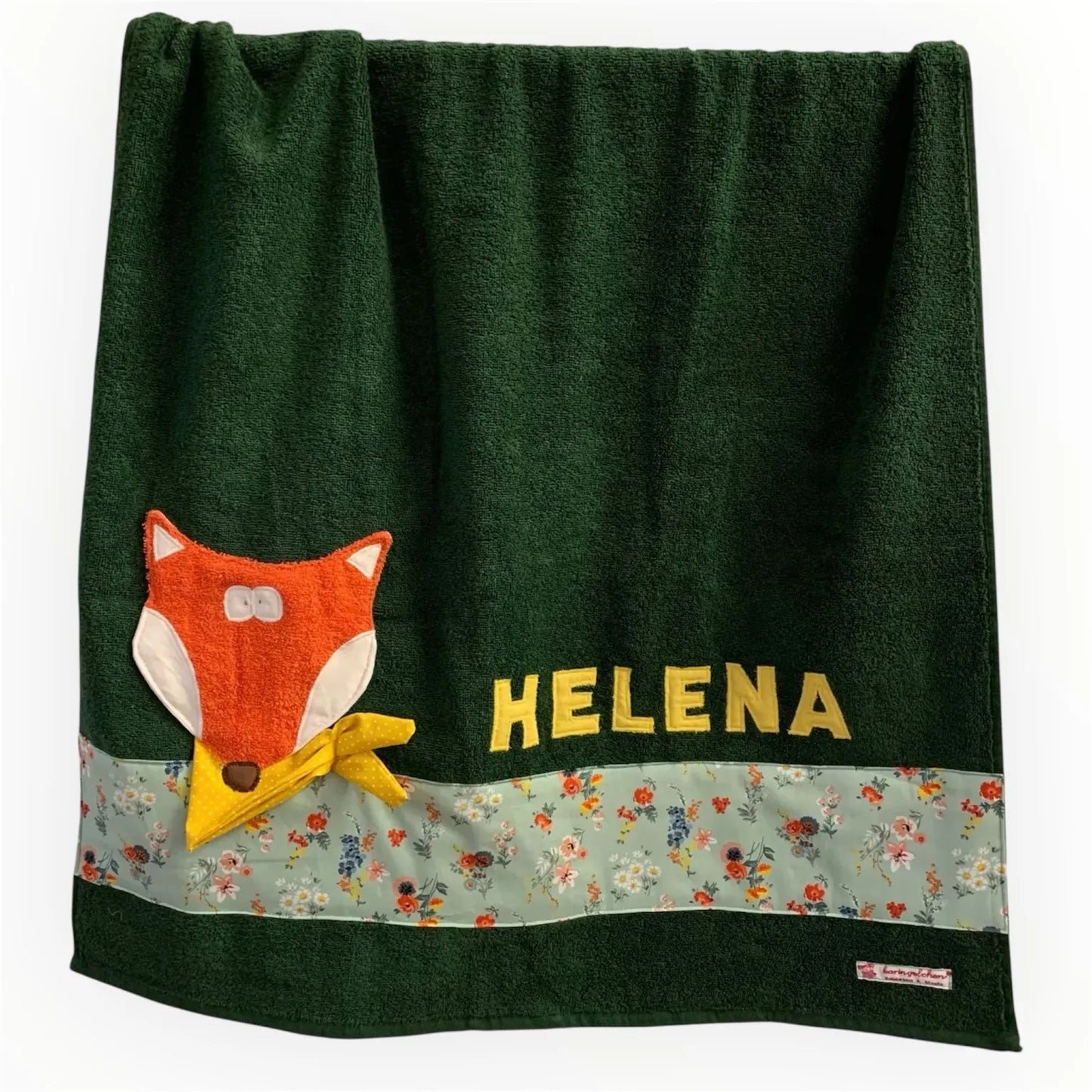Handgemachtes dunkelgrünes Duschtuch mit appliziertem Fuchs in der linken unteren Ecke, personalisiert mit Namen in gelben Buchstaben. Unten am Handtuch ist ein Streifen in altmint geblümt aufgenäht.
