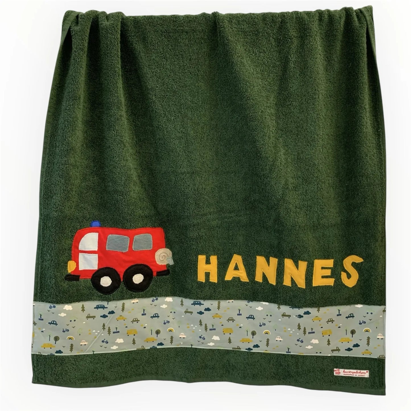 Handgemachtes dunkelgrünes Duschtuch mit applizierter Feuerwehr in der linken unteren Ecke, personalisiert mit Namen in gelben Buchstaben. Unten am Handtuch ist ein Streifen in altmint mit Autoprint aufgenäht.