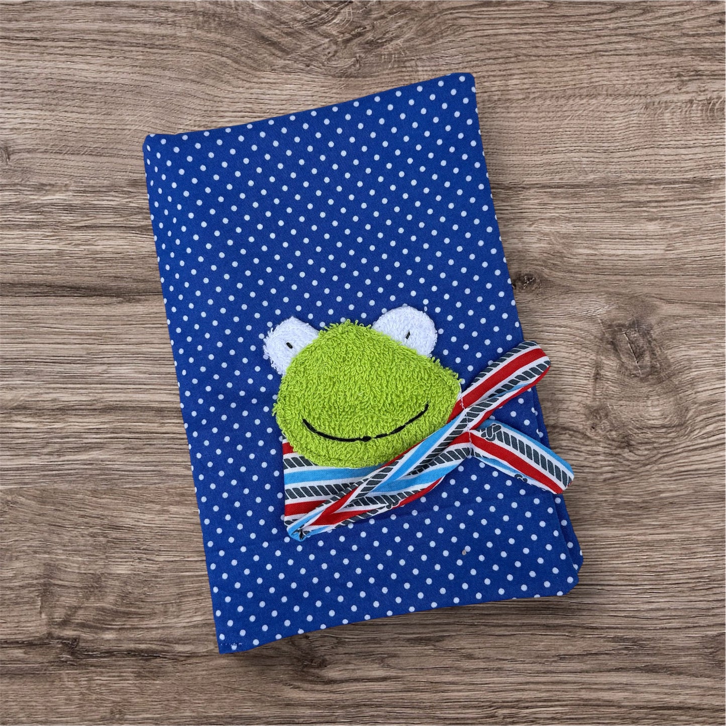 Personalisierbare U-Heft-Hülle aus royalblauen Stoff mit weißen Punkten , verziert mit einem fröhlichen Frosch und personalisierbar mit Namen