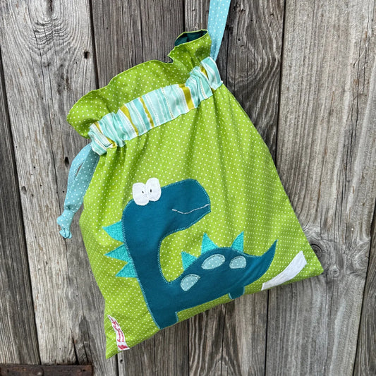 Handgemachter Wetbag für Kinder aus grün gepunktetem Stoff mit niedlicher Dino-Applikation, ideal für Kita, Kindergarten und unterwegs zum Aufbewahren von nasser Kleidung oder Wechselwäsche