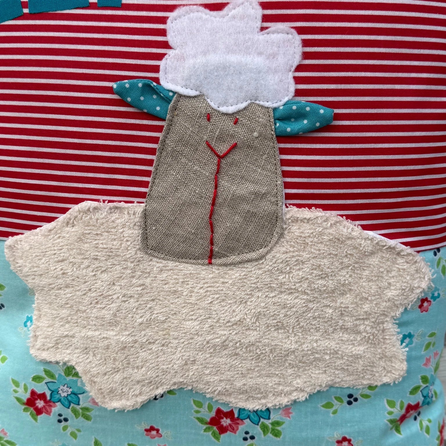 Detailansicht der handgenähten Schaf-Applikationen auf personalisiertem Kinderkissen, strukturierter Stoff mit sichtbaren Ziernähten