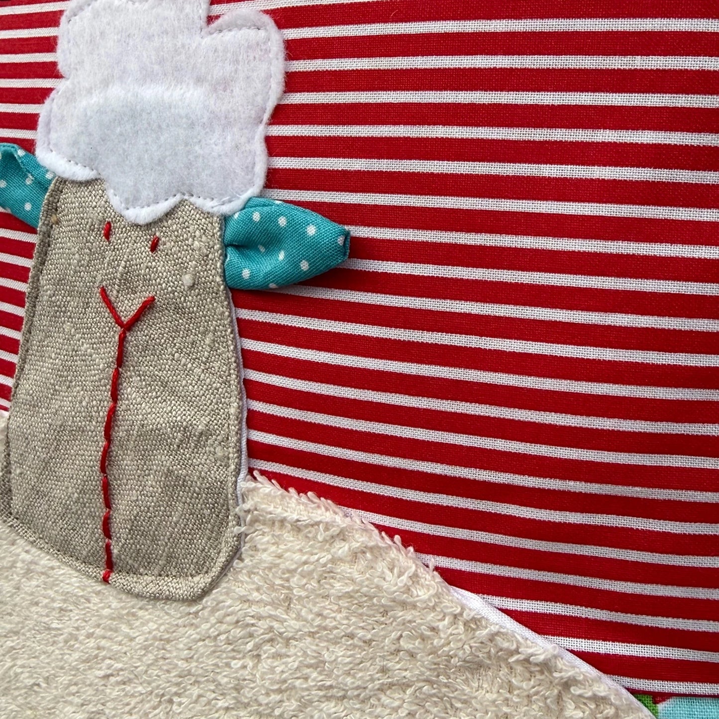 Detailansicht der handgenähten Schaf-Applikation auf Kinderkissen, rot-weiß gestreifter Stoff mit strukturierter Oberfläche und sichtbaren Nähten