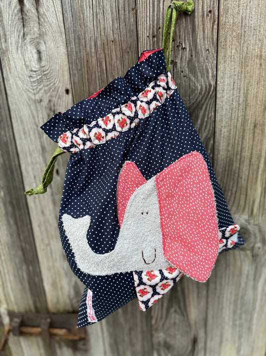 Dunkelblauer Wetbag mit weißen Punkten, verziert mit einer bunten Stoffapplikation einem Elefant .DerBeutel hat einen floralen Tunnelzug  und grüne Kordeln, aufgenommen vor rustikalem Holzhintergrund.