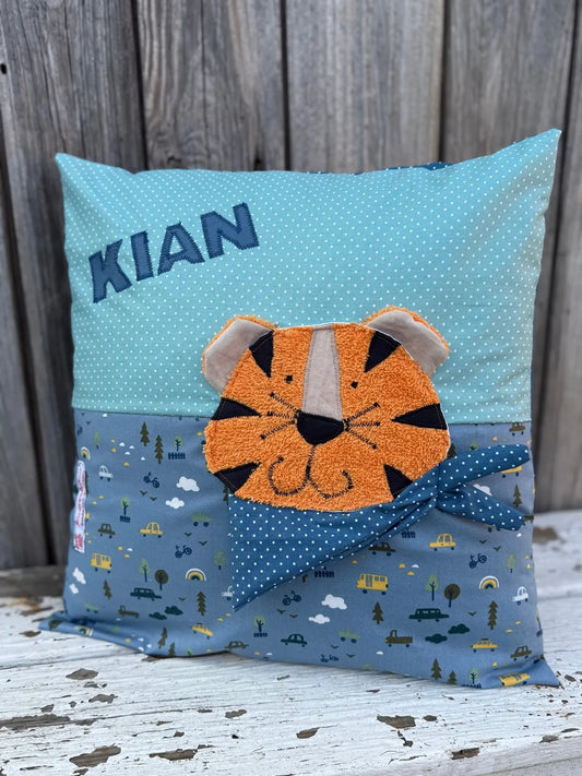 Handgenähtes Kinderkissen personalisiert, gestaltet mint mit weißen Punkten im oberen Teil, blauen  mit 
Autoprint im unteren Teil. Auf dem Kissen ist eine Tiger-Applikation in leuchtendem Orange. Fotografiert vor einem rustikalen Holzhintergrund 