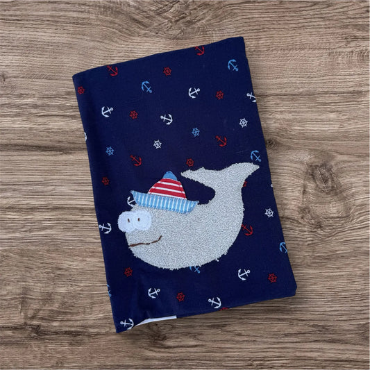 Personalisierbare U-Heft-Hülle aus dunkelblauen Stoff mit maritimen Print verziert mit einem fröhlichen Wal und personalisierbar mit Namen