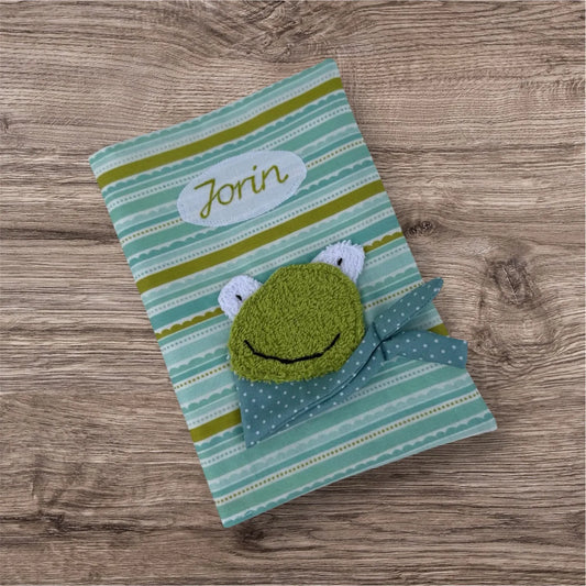 Personalisierbare U-Heft-Hülle aus türkis gestreiften Stoff  , verziert mit einem fröhlichen Frosch und personalisierbar mit Namen