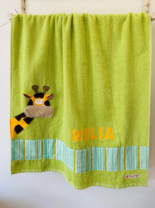 Handgemachtes hellgrünes Duschtuch mit applizierter Giraffe in der linken unteren Ecke, personalisiert mit Namen in gelben Buchstaben. Unten am Handtuch ist ein Streifen in grün blau gestreift aufgenäht.