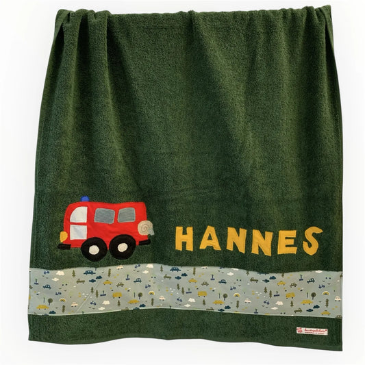 Handgemachtes dunkelgrünes Duschtuch mit applizierter Feuerwehr in der linken unteren Ecke, personalisiert mit Namen in gelben Buchstaben. Unten am Handtuch ist ein Streifen in altmint mit Autoprint aufgenäht.