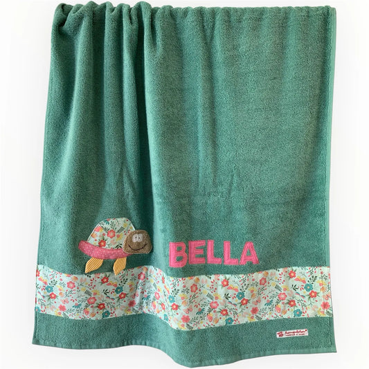 Handgemachtes mintfarbenes Duschtuch mit applizierter Schildkröte in der linken unteren Ecke, personalisiert mit Namen in rosa Buchstaben. Unten am Handtuch ist ein Streifen in bunt geblümt aufgenäht.