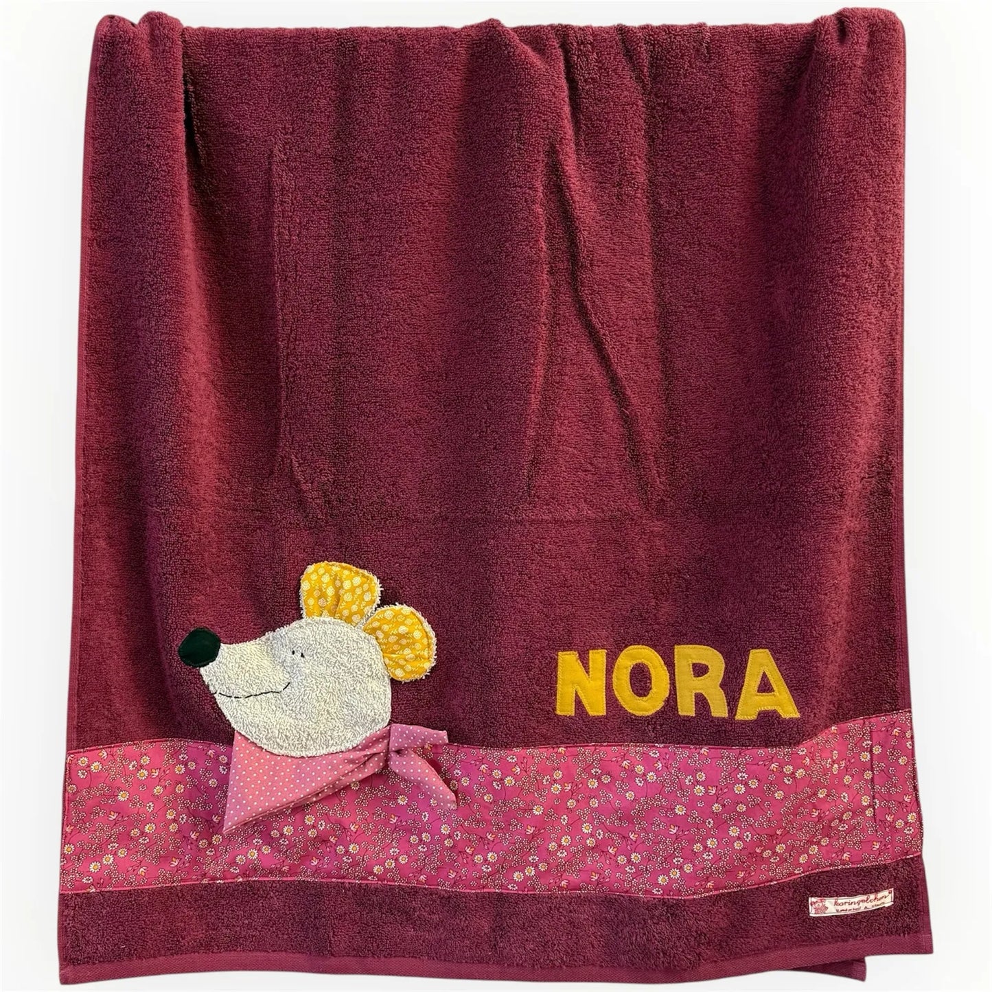Handgemachtes bordeauxrotes Duschtuch mit applizierter Maus in der linken unteren Ecke, personalisiert mit Namen in gelben Buchstaben. Unten am Handtuch ist ein Streifen in beerefarben geblümt aufgenäht.