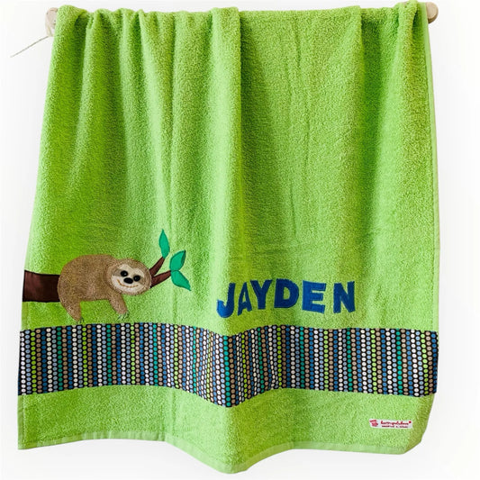 Handgemachtes hellgrünes Duschtuch mit appliziertem Faultier in der linken unteren Ecke, personalisiert mit Namen in gelben Buchstaben. Unten am Handtuch ist ein Streifen in braun grün blau gepunktet aufgenäht.