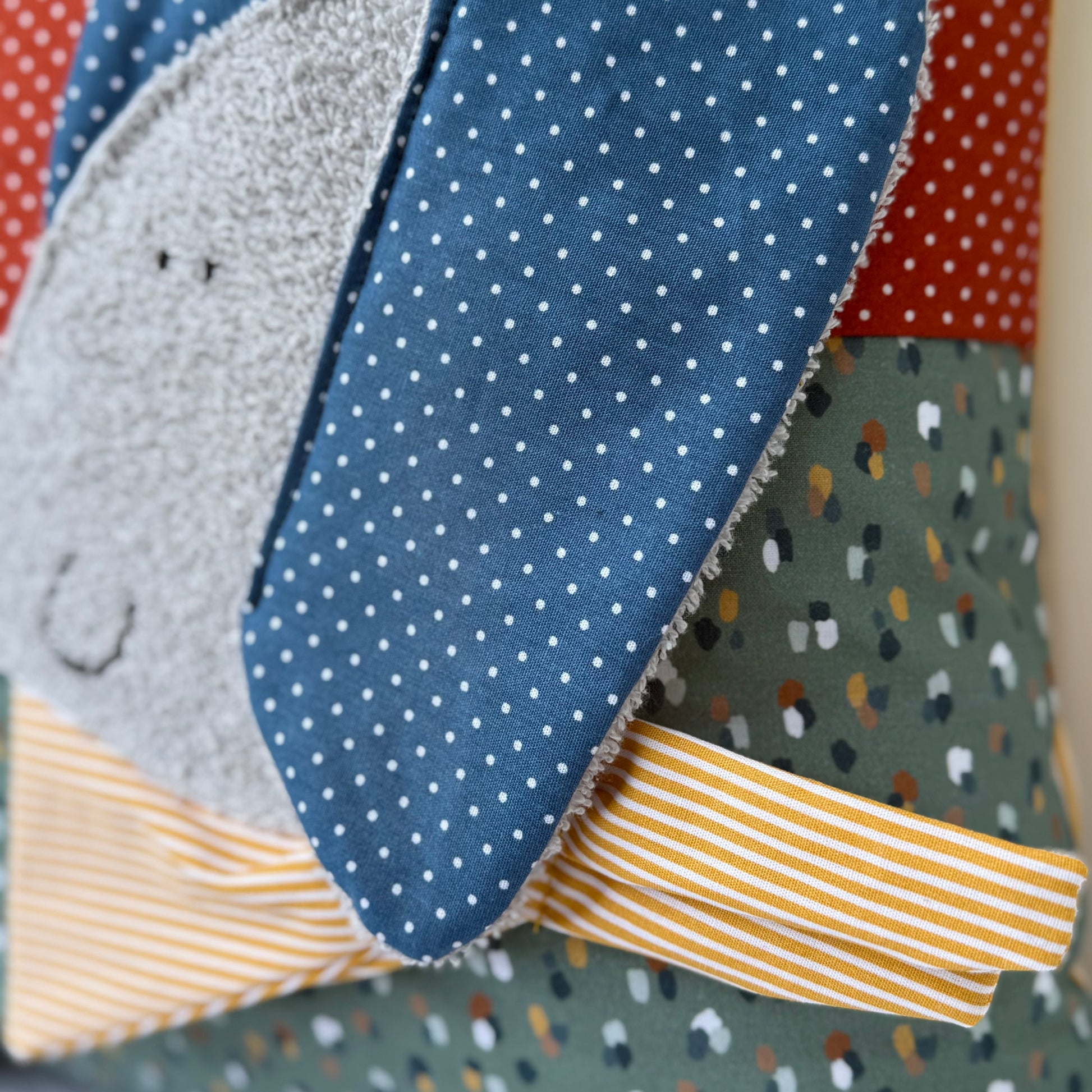 Personalisiertes Kinderkissen mit Elefant und Namen, Rost rot gepunkteter Baumwollstoff und Salbei getupften Baumwollstoff mit 3D-Frottee-Applikation in Blau und Grau, handgemacht.
Seitliche Nahaufnahme der Elefantenapplikation 