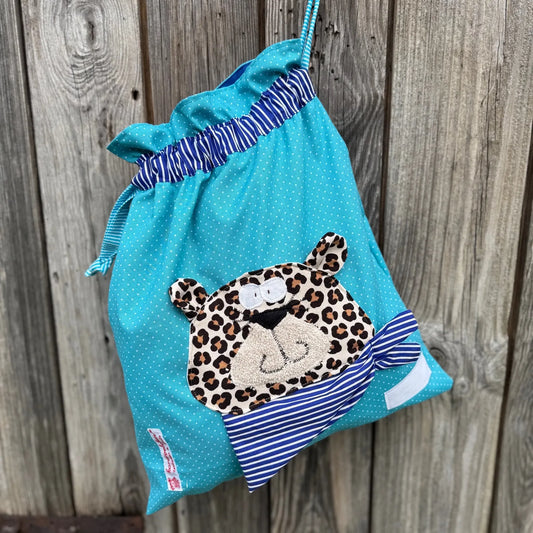 Türkis gepunkteter Wetbag mit aufgenähten Leopard. Der Leopard trägt ein royalblau gestreiftes Halstuch. 
Der Wetbag hat einen Tunnelzug mit Zugbändern. Das Innenfutter ist wasserabweisend. 